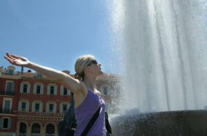Girl stands with arms wide in front of water fountain in Nice, France