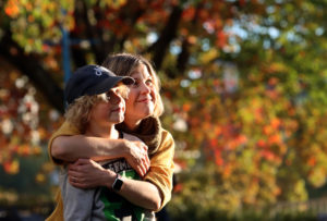 Mom hugs son with colourful fall trees and leaves in the background