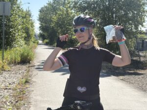 Katie stopped, sitting on her bike, holding up a bag of gummies and a bag of RxBar squares in one hand, and in the other, one Rx square between two fingers.