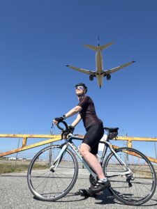 Katie seated on her bike with a airplane flying overhead.