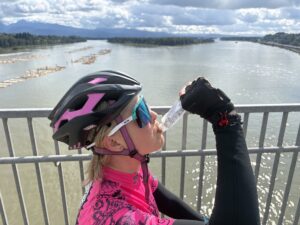 A female cyclist eats apple sauce from an apple sauce pouch while on her bike