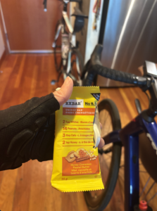A cyclist holds an RXBAR in her hand with 2 road bikes in the foreground